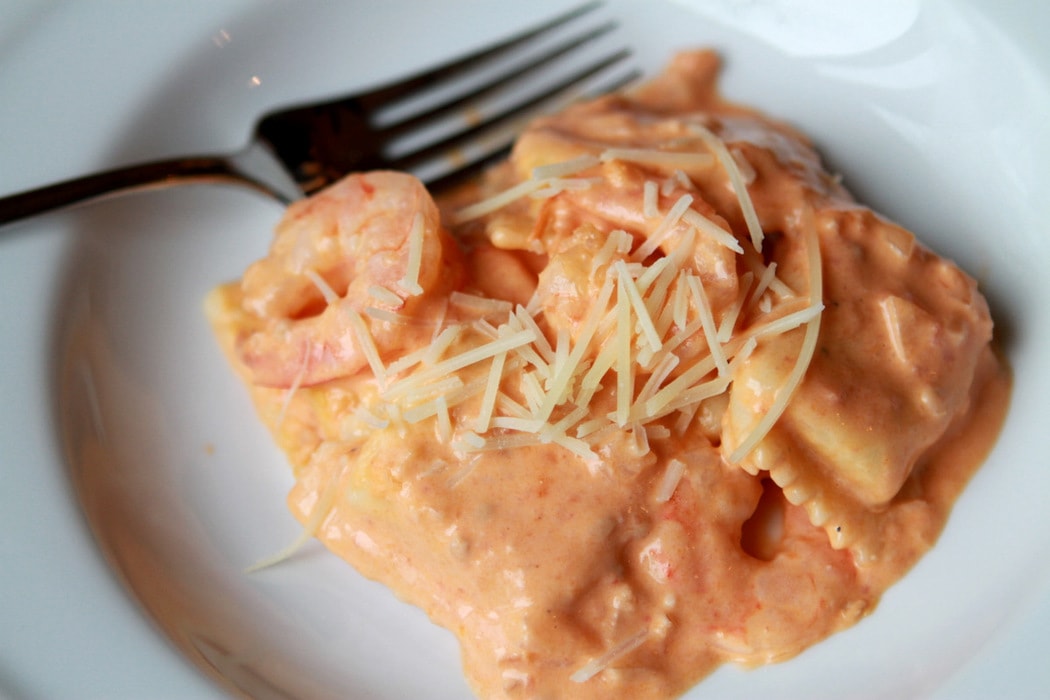 shrimp and ravioli topped with pink sauce in a white dish.