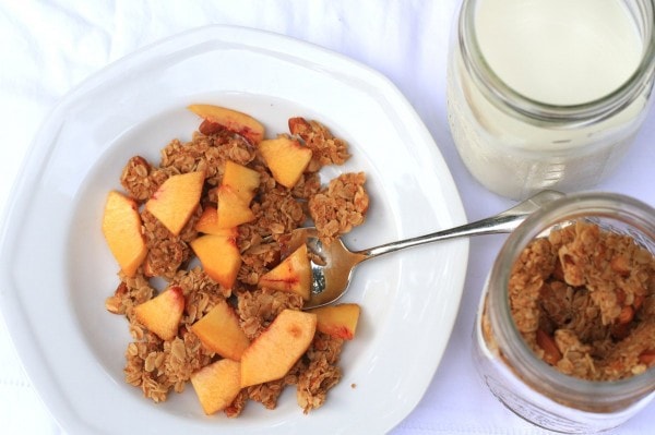 A bowl of granola, topped with sliced peaches, in a white bowl.