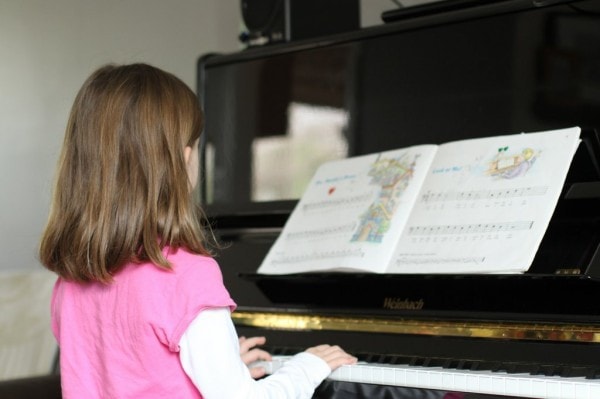 A little girl in a pink shirt practicing piano.