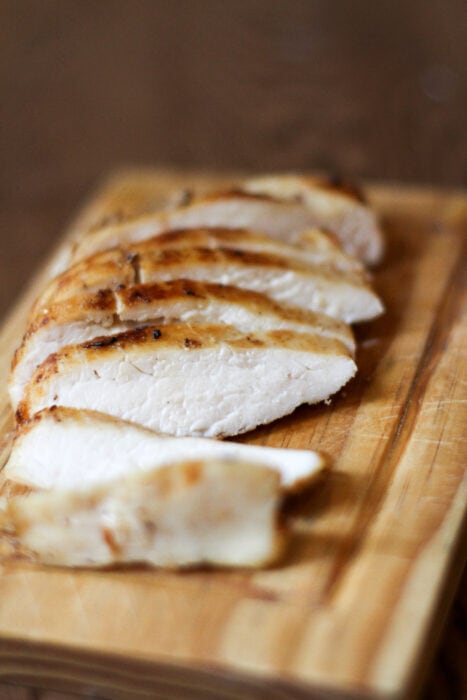 Brineraded, sliced chicken breast on a wooden cutting board.