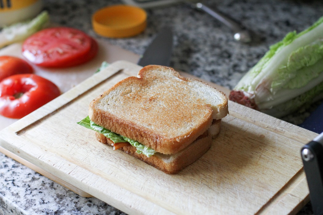 A grilled BLT sandwich on a wooden cutting board.