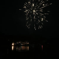 Fireworks exploding in a night sky over a river.