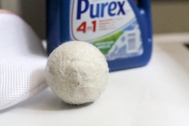 wool dryer ball in front of a Purex laundry detergent container.